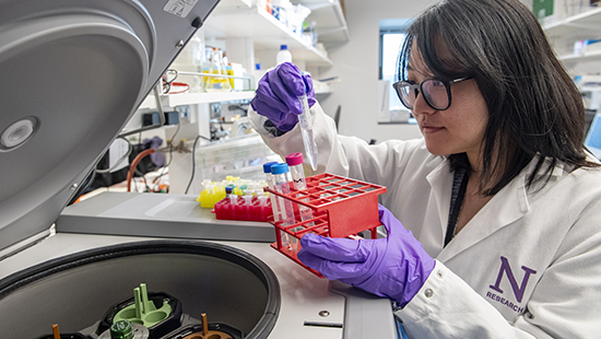 woman in lab coat looking at vials in lab setting
