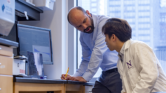 Daniel Arango writing on paper and discussing with lab member
